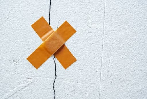 An adhesive bandage taped over a crack in a white wall, illustrating a cosmetic patch rather than a structural repair