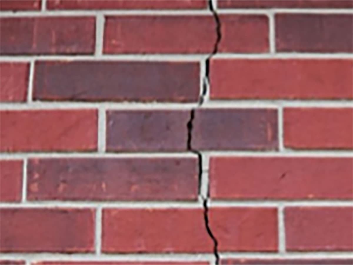 Stair-step crack running through the mortar joints of a brick exterior wall, a common sign of foundation settlement